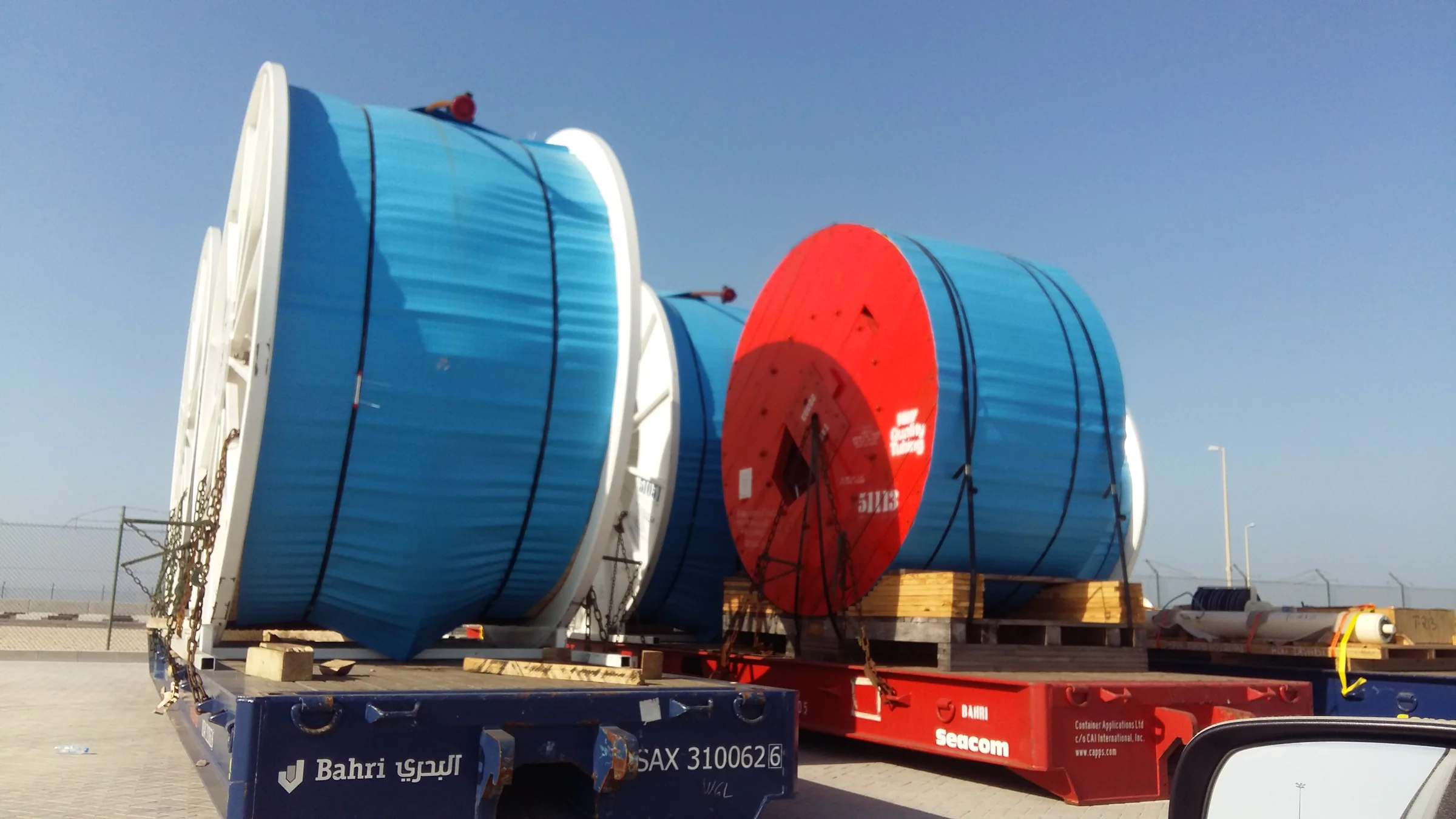 Large blue cable reels fastened on transport trailers.