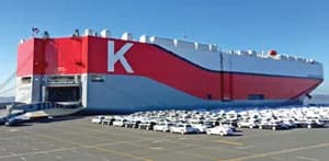 Large car carrier ship with parked vehicles alongside.