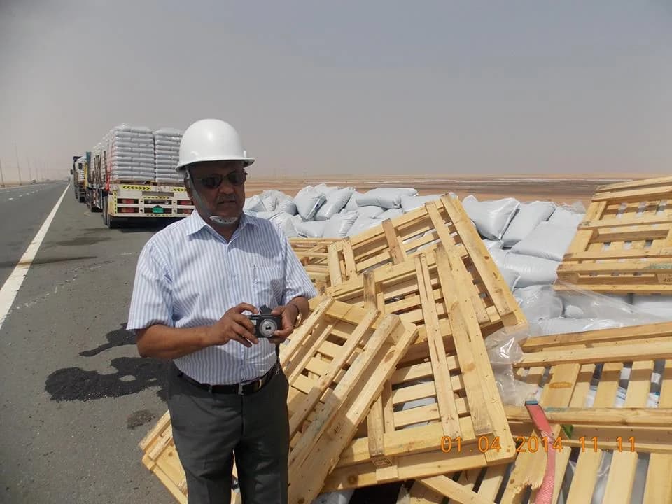 Surveyor beside damaged wooden pallets and bagged cargo along a road.