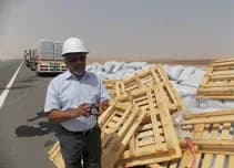 Small archival view of a surveyor beside pallets and bagged cargo.