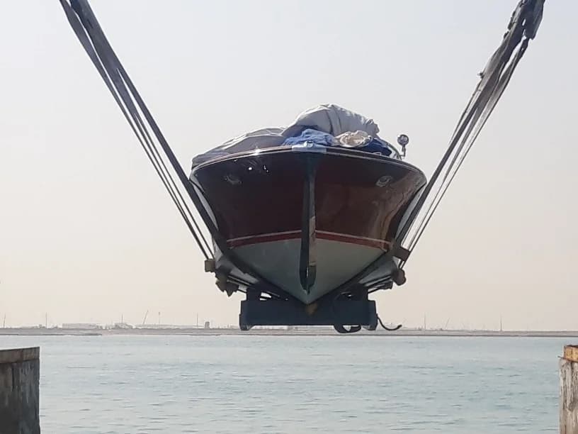 Small motorboat suspended by lifting straps above the water.