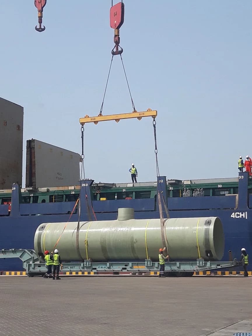 Large cylindrical tank rigged to a spreader bar beside a vessel.