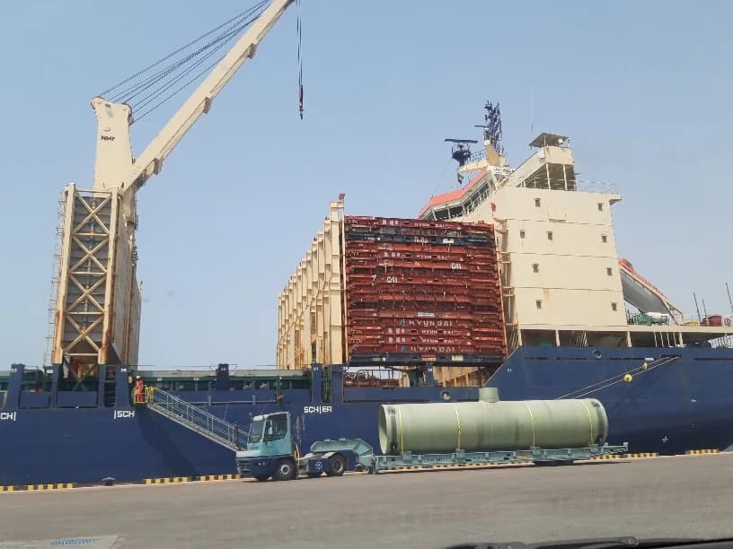 Cylindrical tank on a trailer beside a cargo ship.