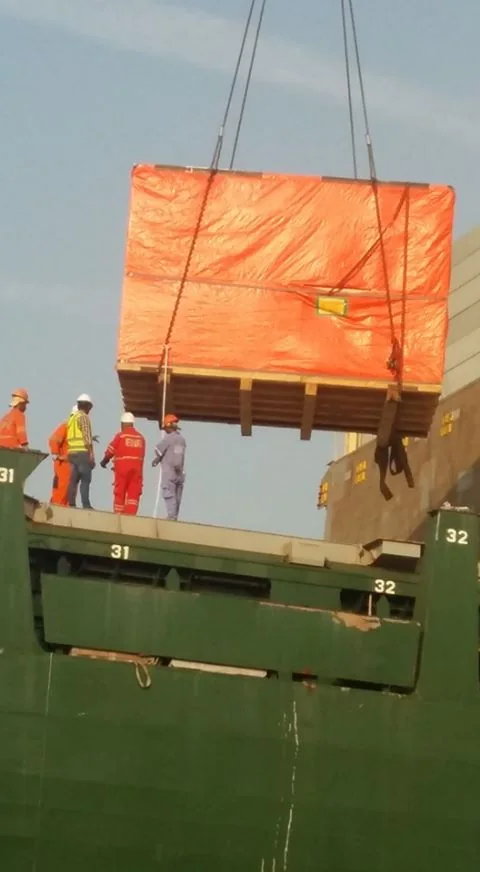 Orange wrapped cargo suspended above an open ship hold.