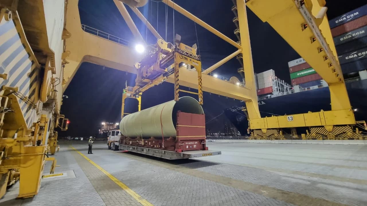 Crane lifting cylindrical project cargo at a port at night.