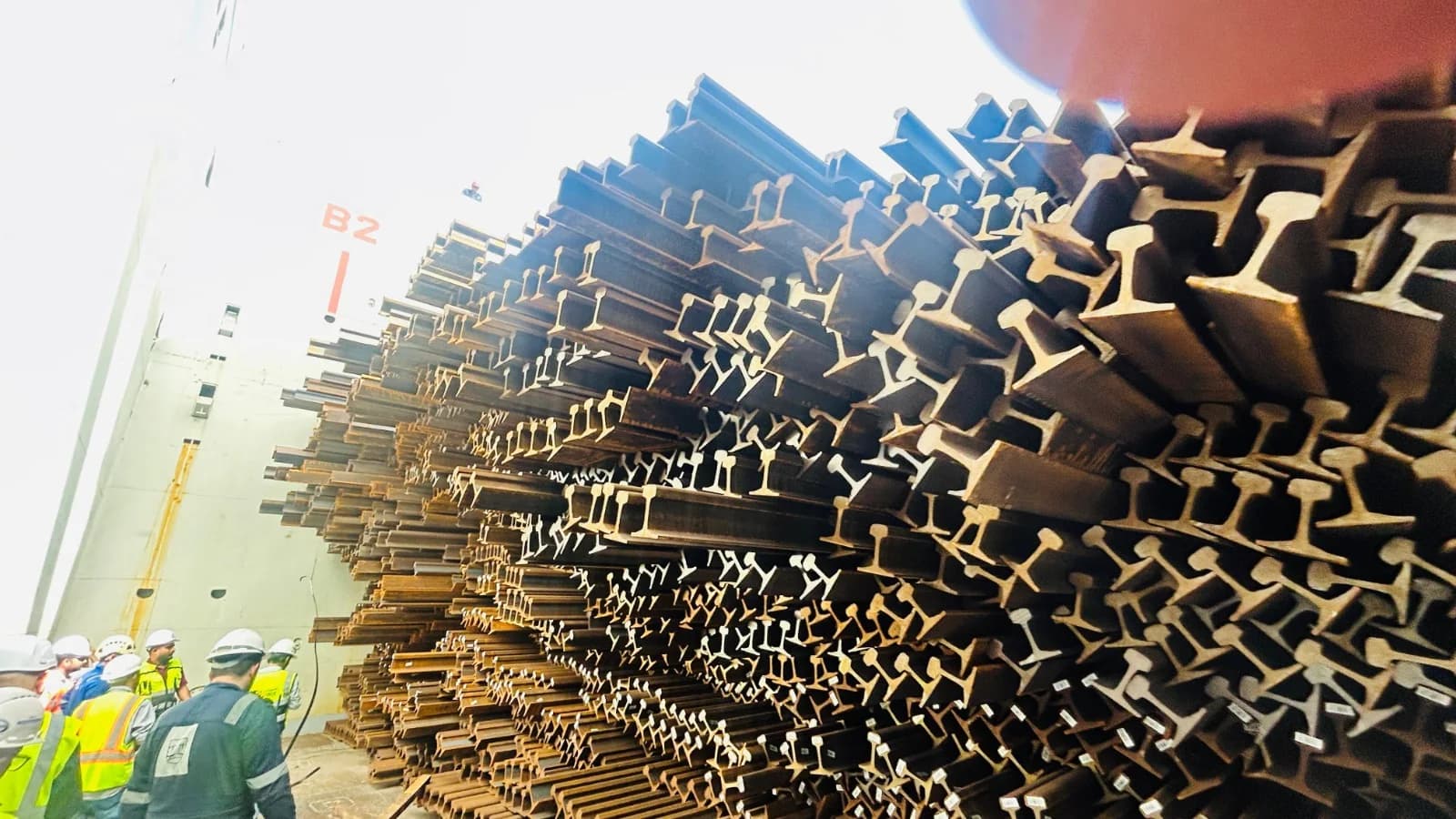 Workers examining stacks of steel cargo.